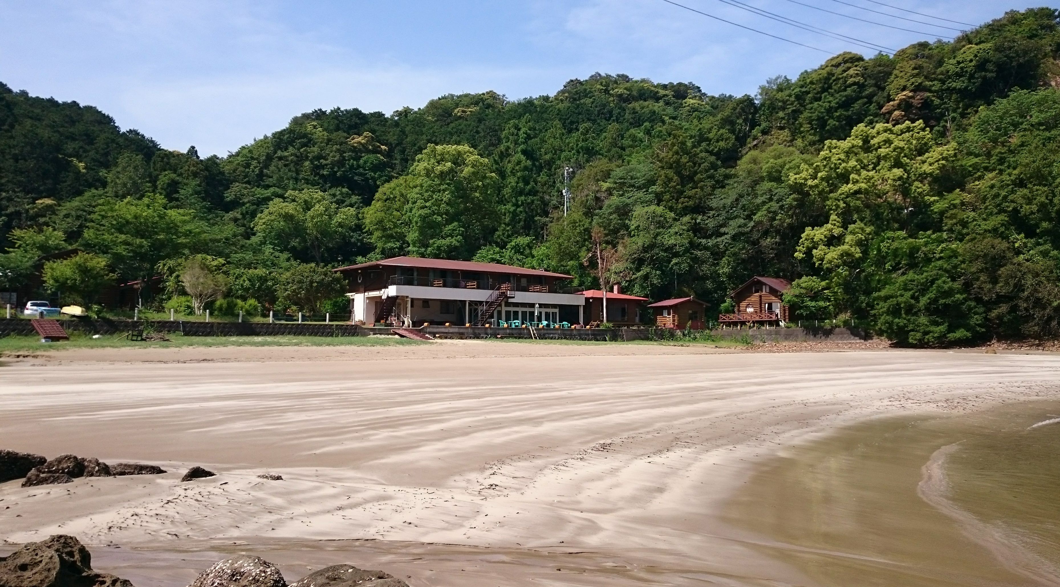A beachside hotel with a large building and smaller cabins, surrounded by dense forest.