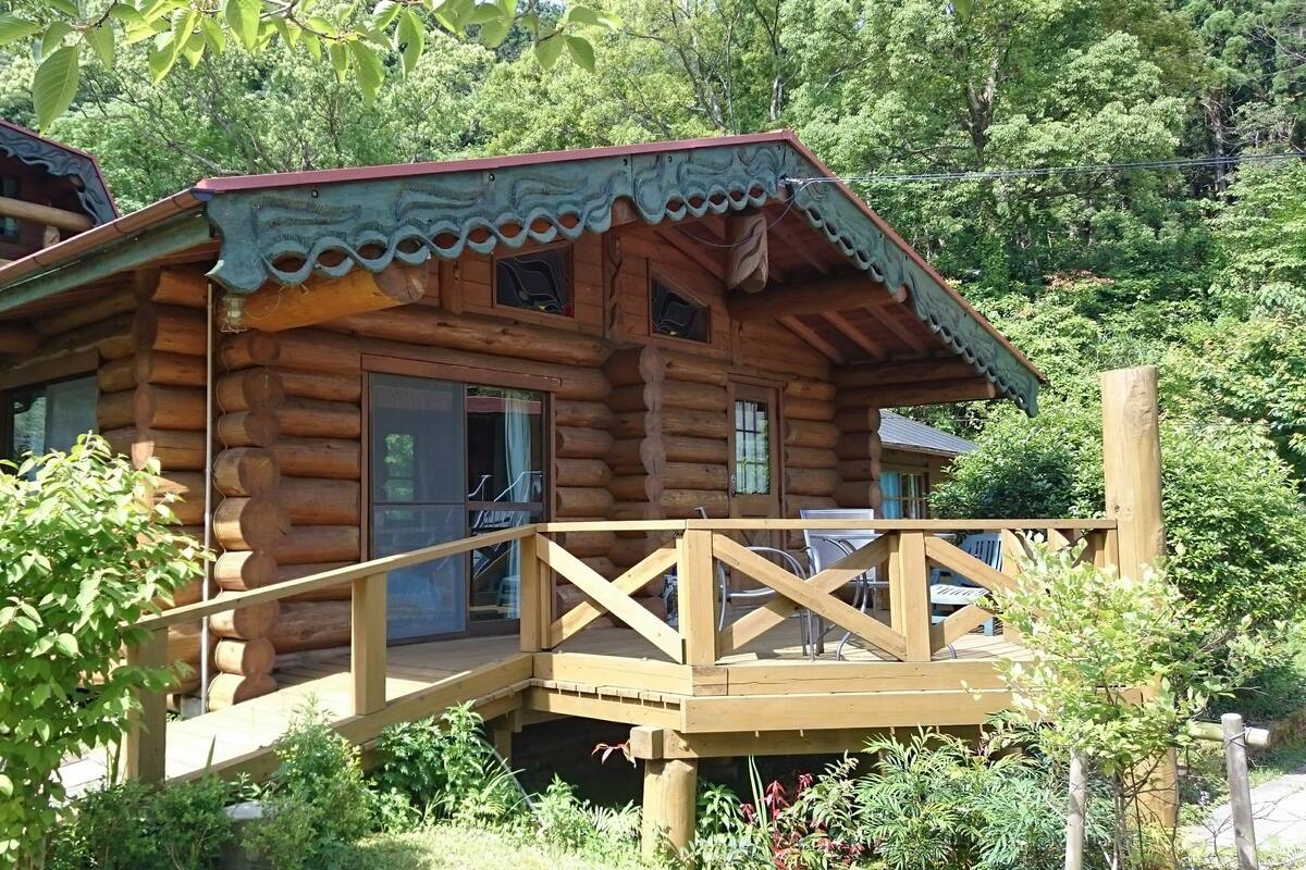 A wooden log cabin with a wooden deck and a staircase leading to the entrance.
