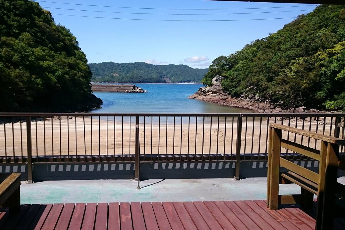 A wooden deck with a metal railing overlooking a beach and a body of water.