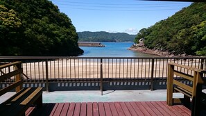 A wooden deck with a metal railing overlooking a beach and a body of water.