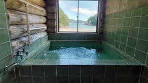 A log cabin bathroom with a wooden interior, a window with a view of a beach, and a bathtub. - Pension Shishikui (Kaiyo)