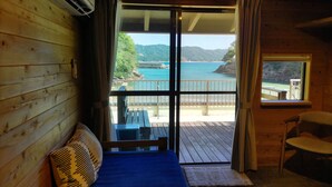 A wooden cabin room with a large sliding glass door leading to a deck with a view of a coastal landscape. - Pension Shishikui (Kaiyo)