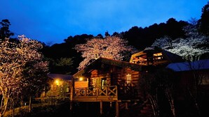 A wooden cabin with a balcony, surrounded by trees and illuminated by warm lights. - Pension Shishikui (Kaiyo)
