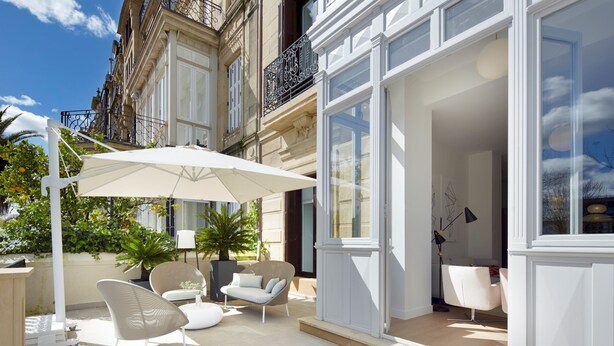 A modern outdoor patio with white furniture, a large umbrella, and potted plants. - La Dolce Vita by FeelFree Rentals (San Sebastián)