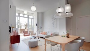A modern living room with a wooden dining table, white chairs, a sofa with colorful cushions, and pendant lights. - La Dolce Vita by FeelFree Rentals (San Sebastián)