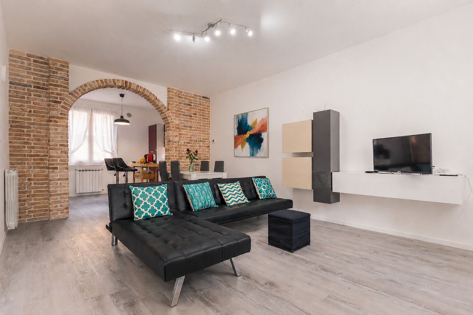 Uma sala de estar moderna com um sofá preto, uma televisão sobre um suporte branco e uma parede de tijolos.