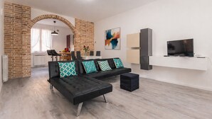 A modern living room with a black sofa, a TV on a white stand, and a brick wall.
