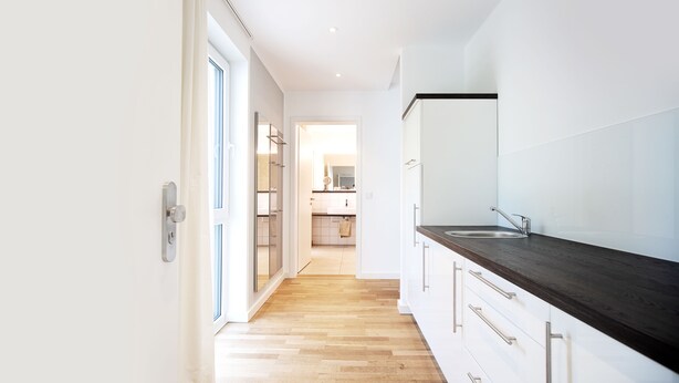 Una cocina moderna con armarios blancos, encimera oscura y suelo de madera.