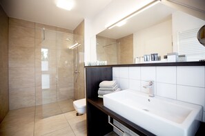 Un baño moderno con cabina de ducha de vidrio, un lavabo blanco y un espejo grande.