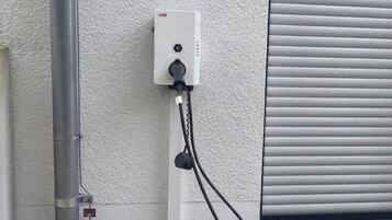 A utility box with a cable connected to a metal pipe and a window with closed blinds.
