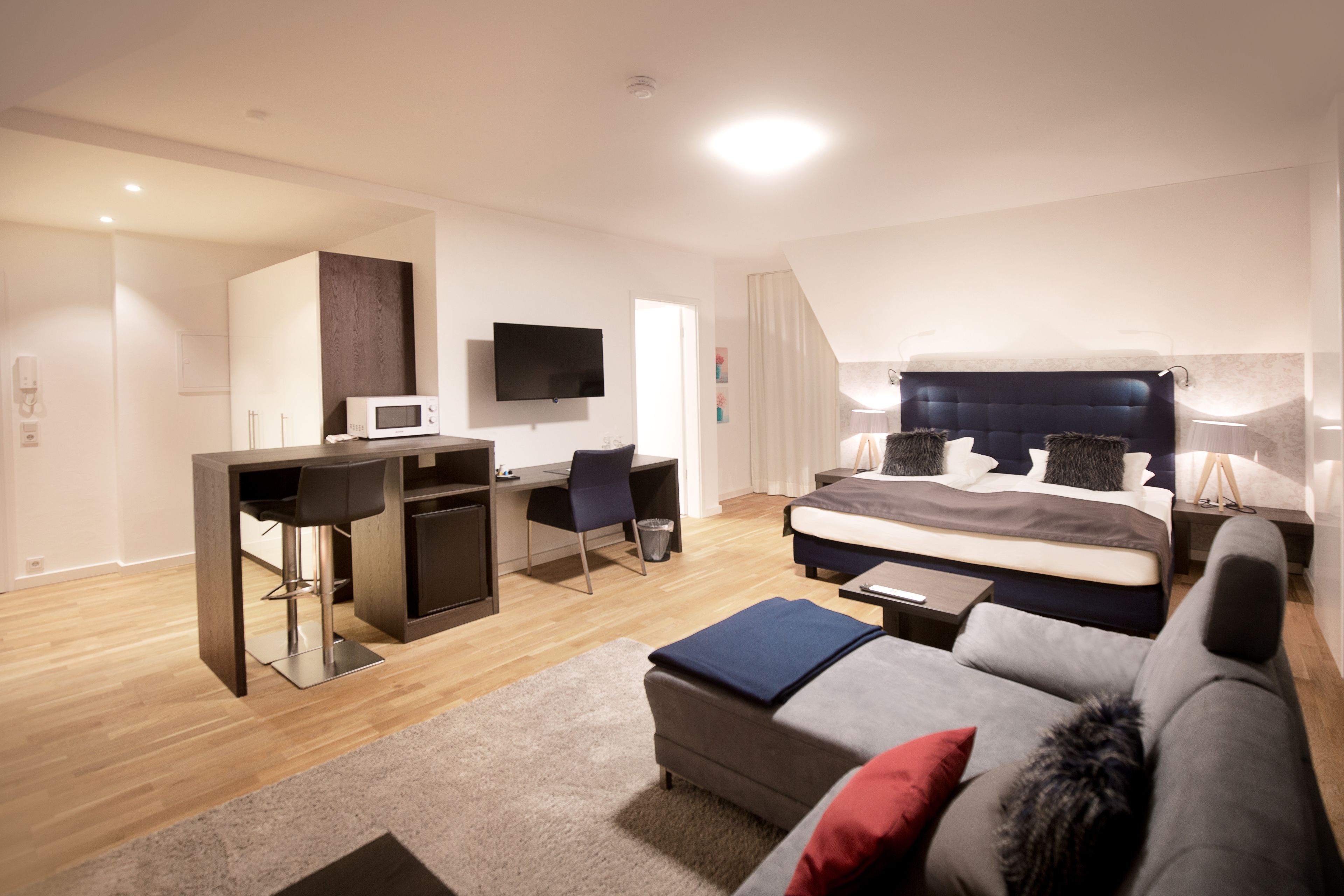 Ein modernes Hotelzimmer mit einem Bett, einer Couch, einem Schreibtisch mit Stuhl, einem Fernseher und einer Mikrowelle.