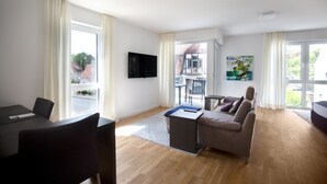 Una sala de estar moderna con un sofá, un televisor instalado en la pared y un comedor con mesa y sillas.