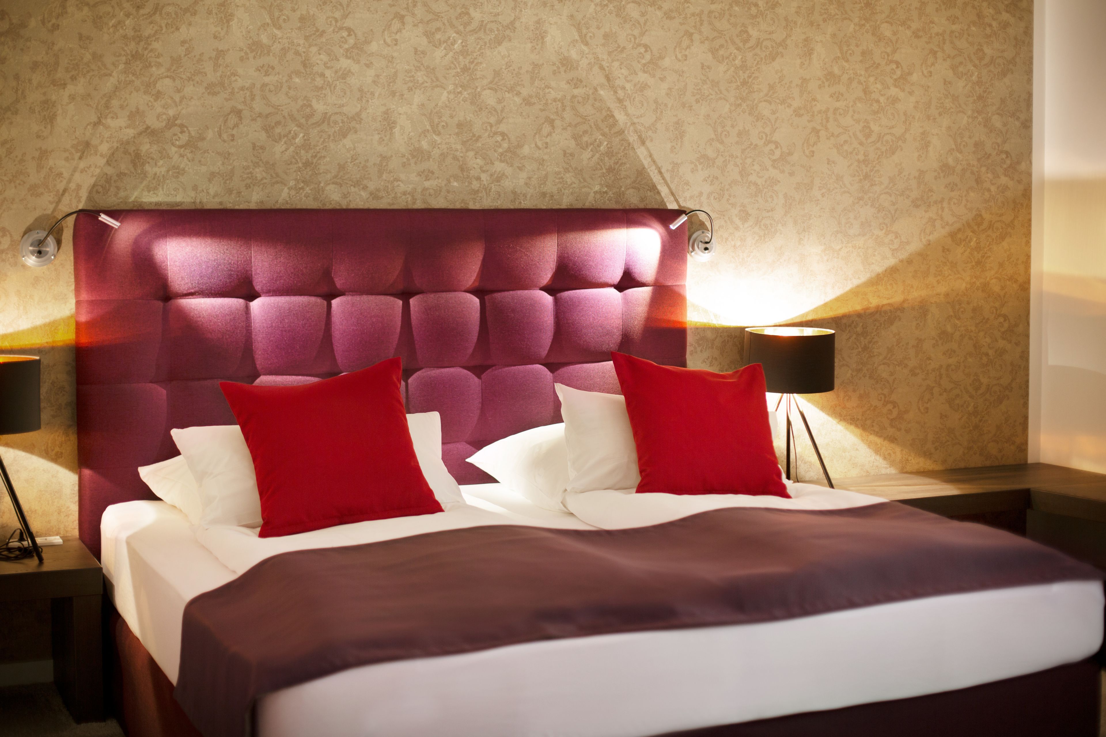 A hotel room with a tufted headboard, a bed with white and red bedding, and two bedside lamps.