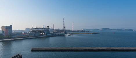 Ein Yachthafen mit vertäuten Booten, ein großes Schiff und Industriegebäude im Hintergrund.