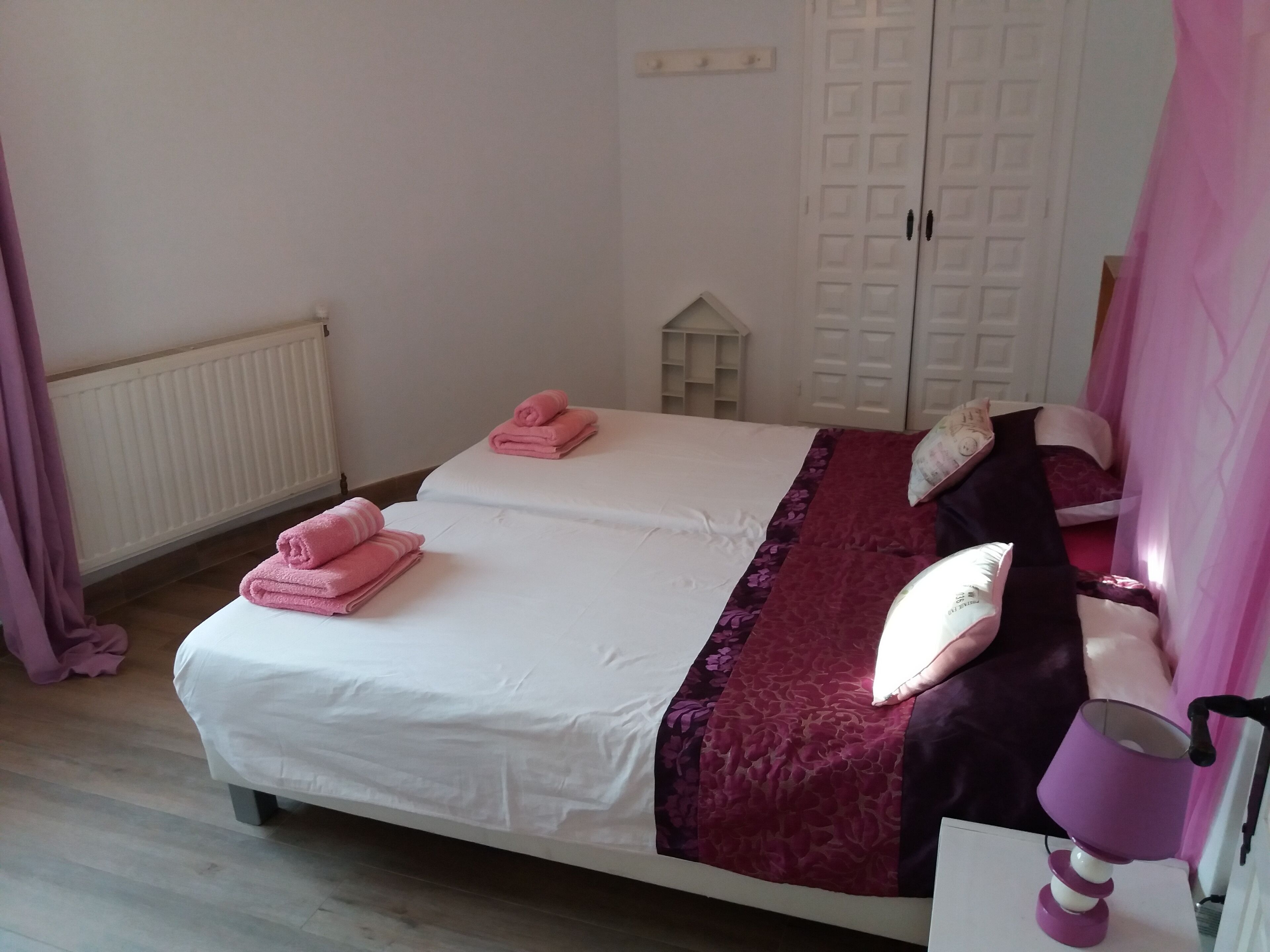 Une chambre avec deux lits, un radiateur, une armoire et une lampe de chevet.