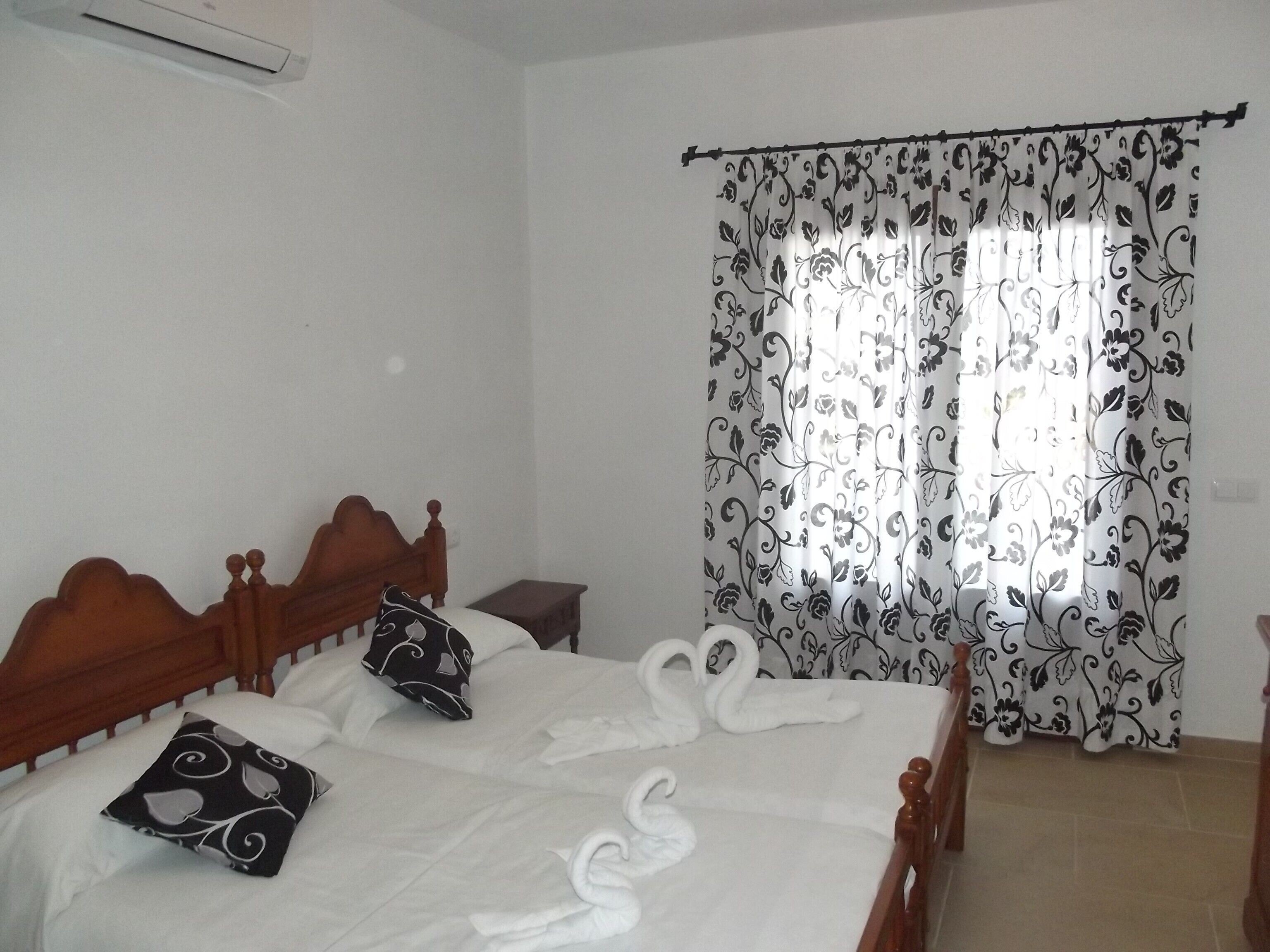 A neatly made bed with a floral-patterned curtain, a wooden headboard, and a small bedside table.