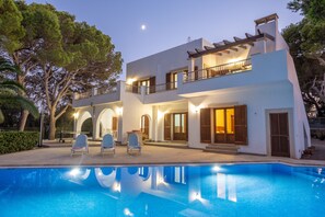 Una casa moderna de dos pisos con piscina, mobiliario exterior y un balcón.