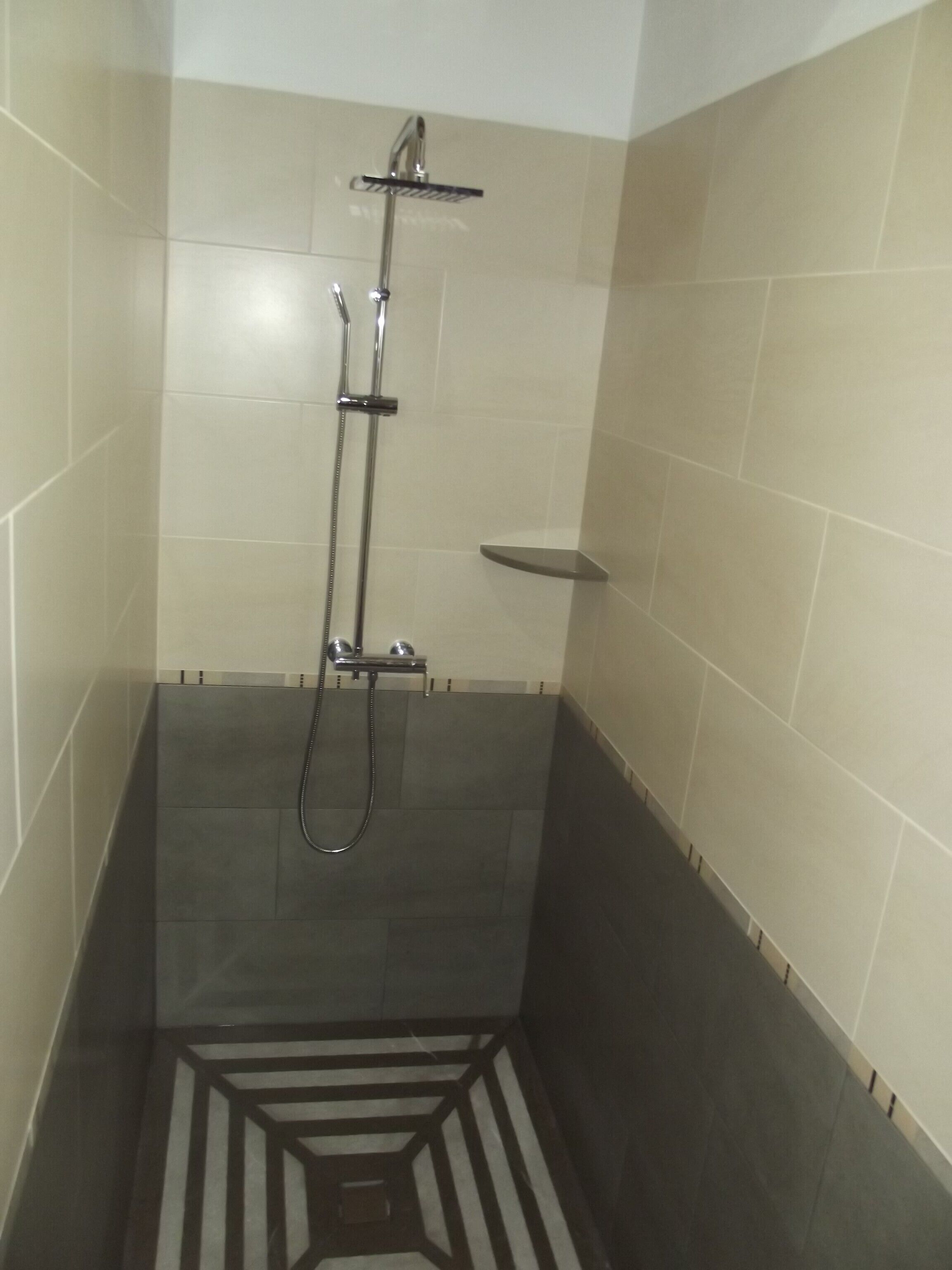 A shower area with a tiled floor and walls, a showerhead, and a handheld shower attachment.