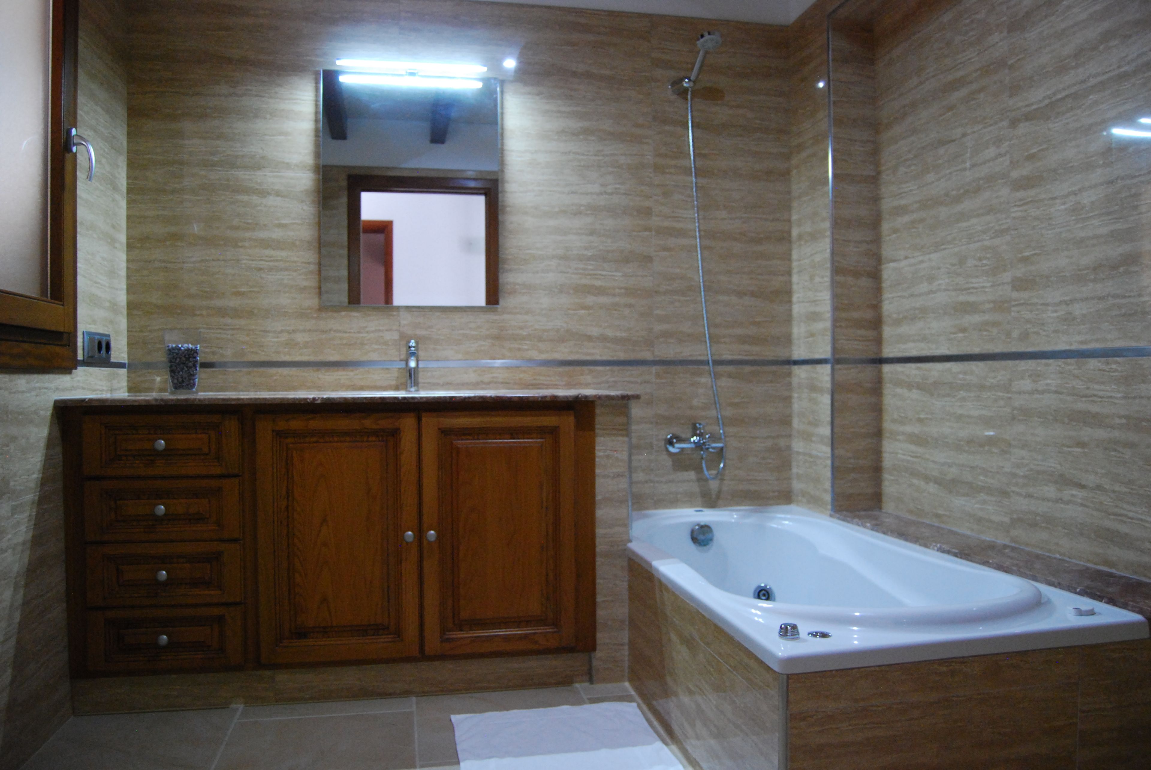 Un baño con tocador de madera, un espejo, una bañera y una ducha.