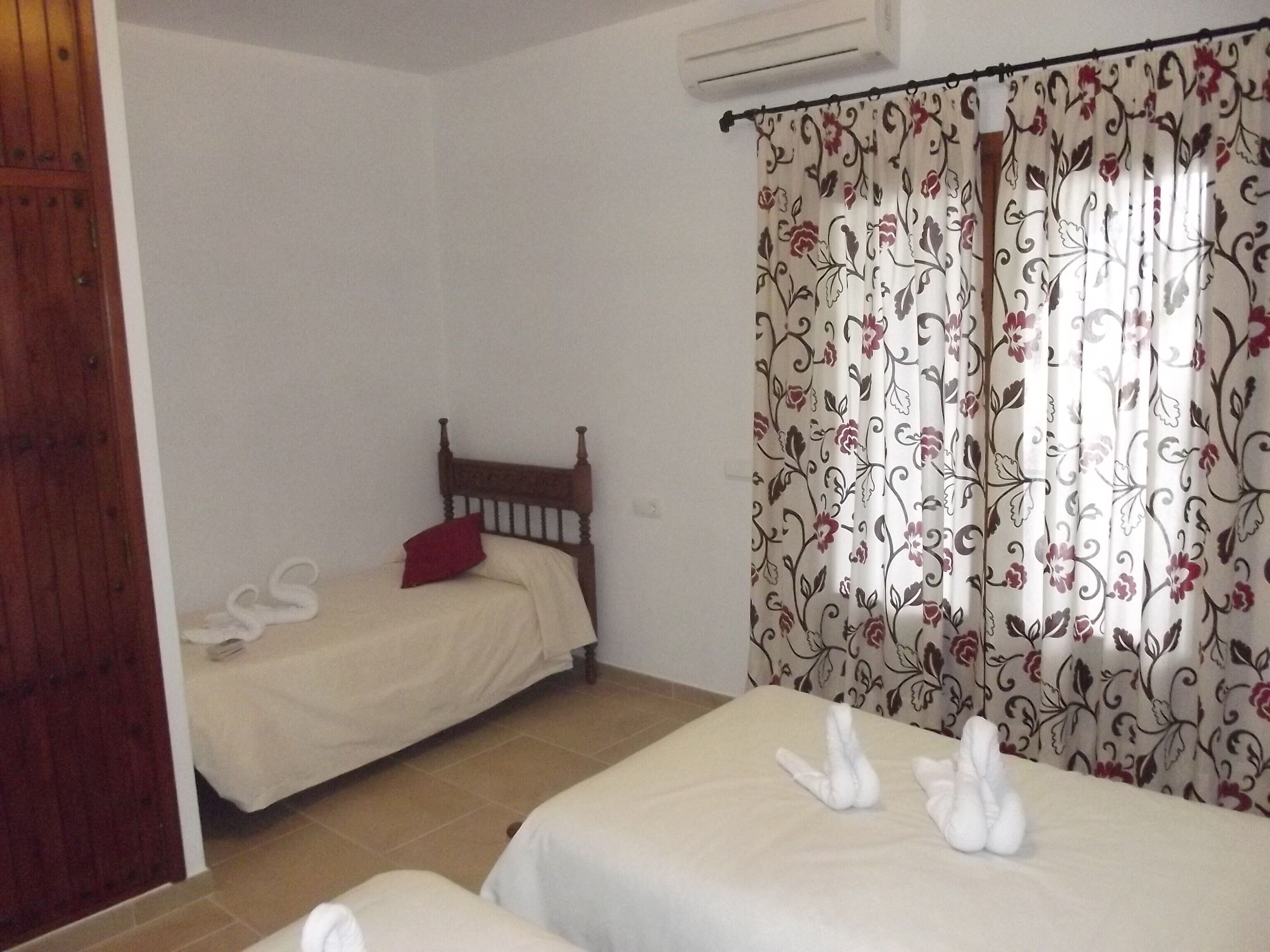 Un dormitorio con dos camas, cabecero de madera, almohada roja y cortinas estampadas.