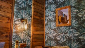 Een houten interieur met een wandlamp, een lijst met spiegel en een tafel met een open boek en brillen.