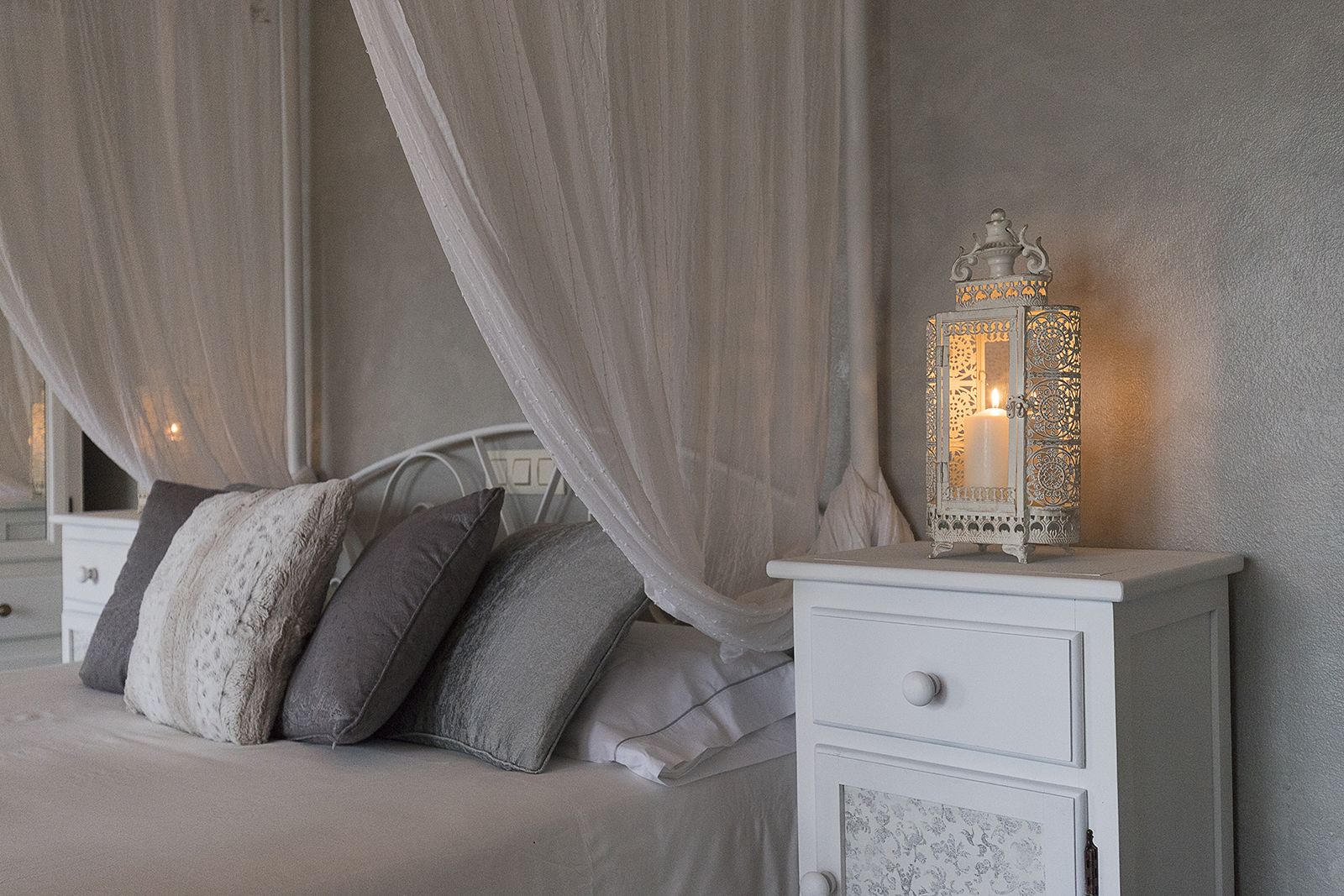 Quarto com cama, mesa de cabeceira, abajur e dossel.