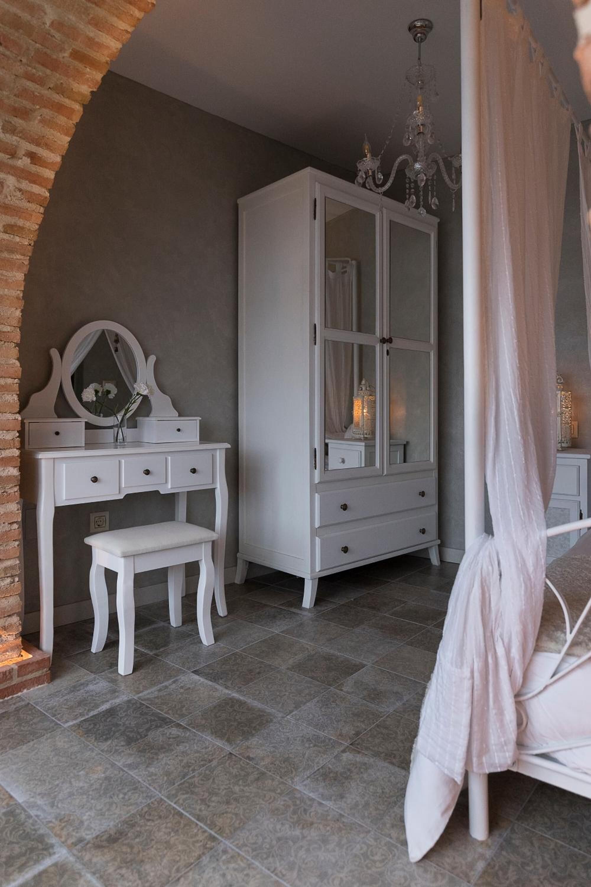Ein Schlafzimmer mit weißem Schminktisch, einem großen Bogenfenster, einem Baldachinbett und einem hohen Kleiderschrank.