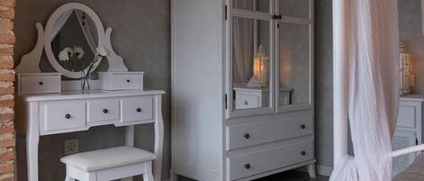 Ein Schlafzimmer mit weißem Schminktisch, einem großen Bogenfenster, einem Baldachinbett und einem hohen Kleiderschrank.