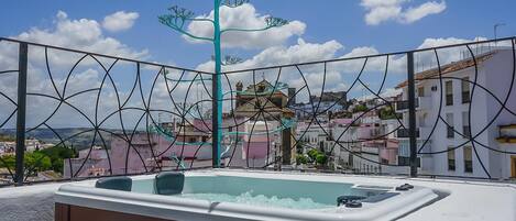 Una terraza con un jacuzzi, un árbol decorativo y vistas a una ciudad con edificios.
