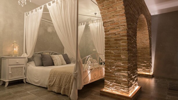Een slaapkamer met een hemelbed, nachtkastje en een kroonluchter.