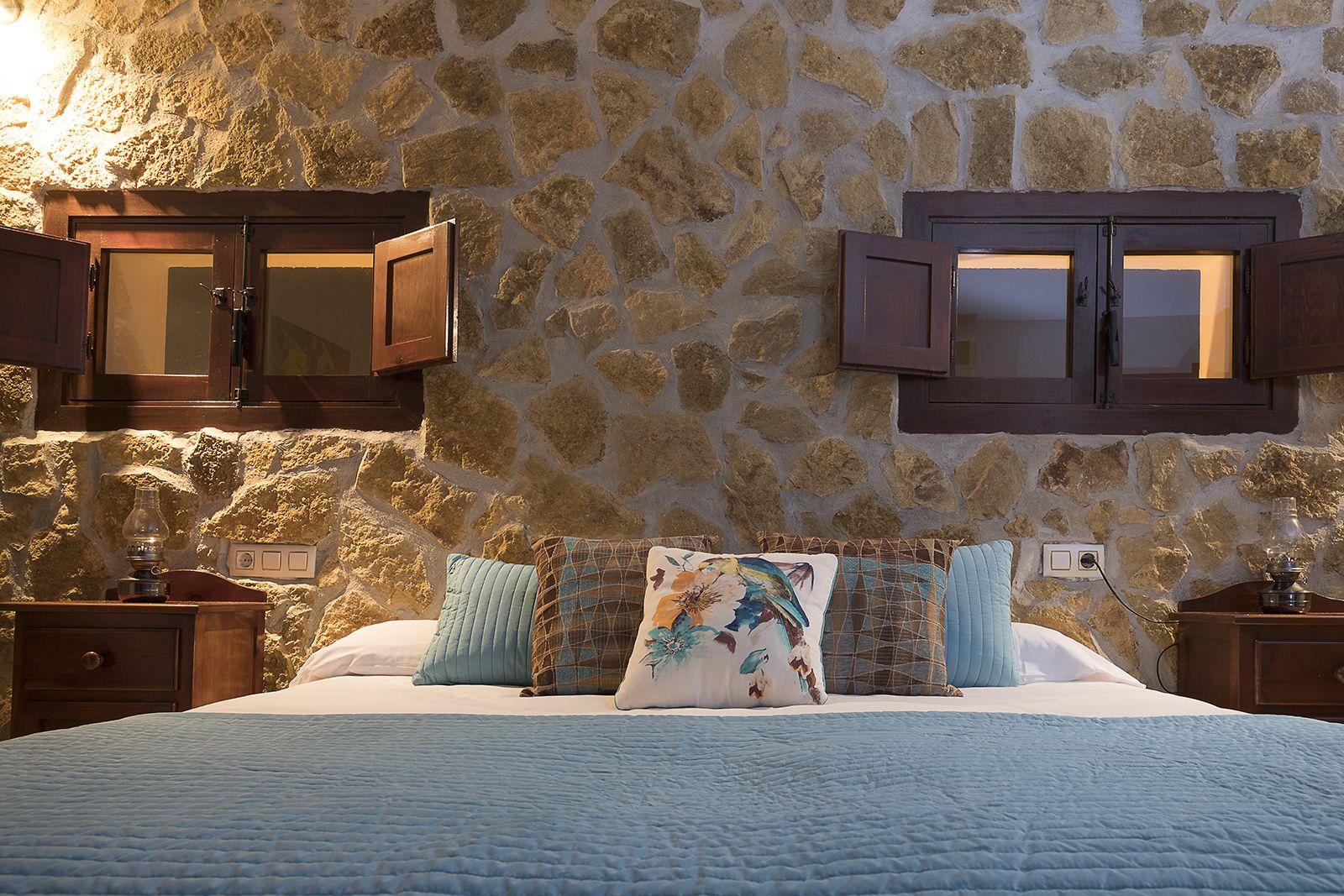Une chambre avec un mur en pierre, un lit recouvert d’une courtepointe et deux armoires en bois.