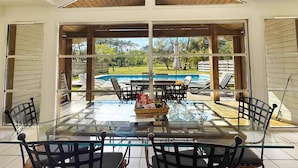 A glass-enclosed patio with a pool view, outdoor furniture, and a table with snacks. - Villas La Clairière aux Chevreuils (Moliets-et-Maa)
