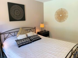 Una cama bien hecha con almohadas estampadas, una lámpara de noche y dos adornos de pared.