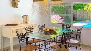 A dining area with a glass table, woven chairs, and a view of a garden through a window. - Villas La Clairière aux Chevreuils (Moliets-et-Maa)