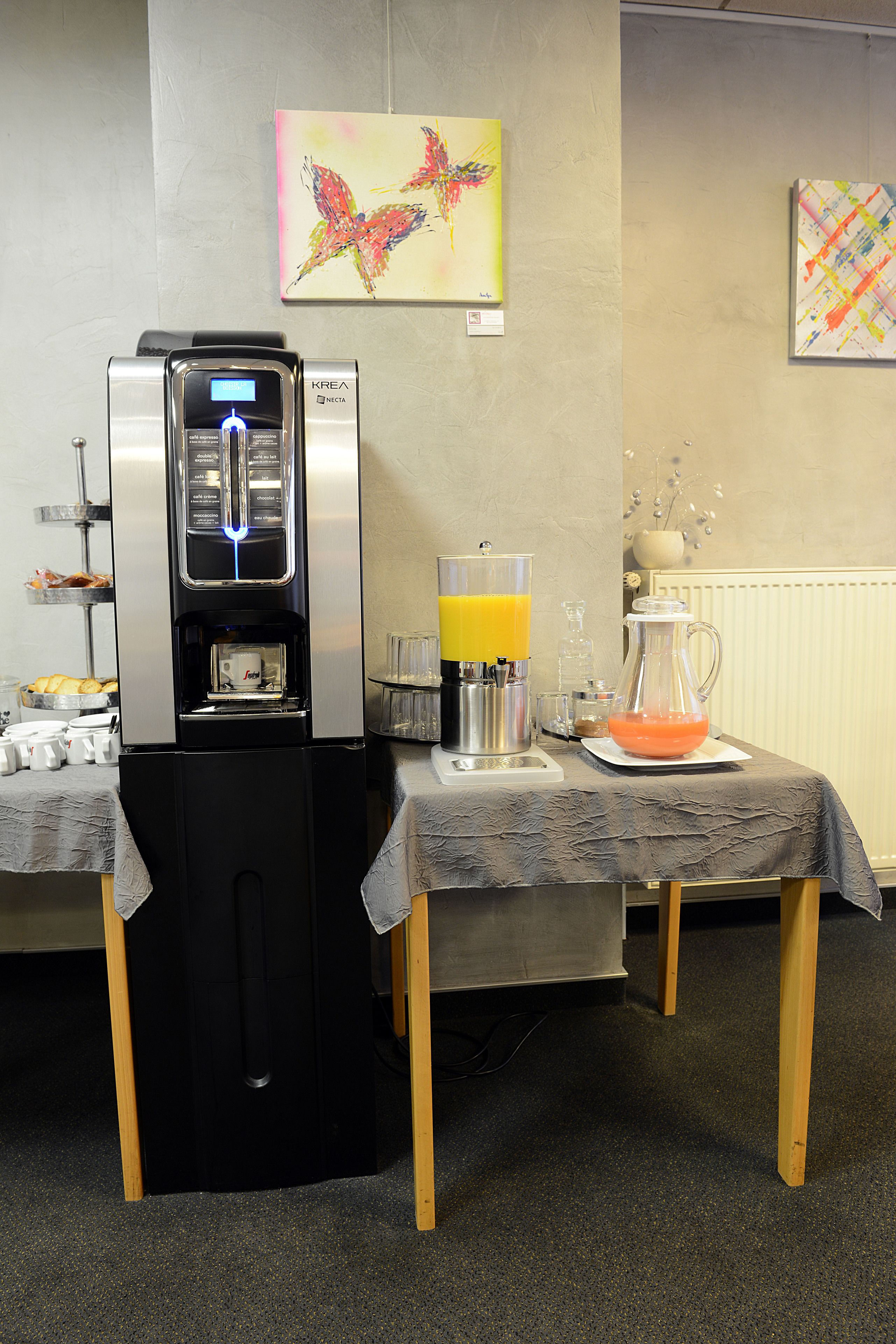 A coffee machine, a juice dispenser, and a pitcher of orange juice on a table with a tablecloth.