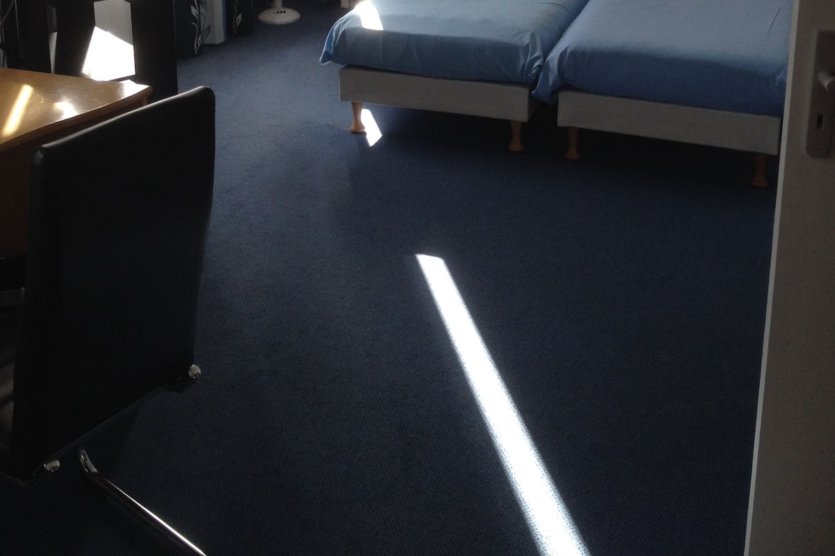 Une chambre d’hôtel avec deux lits, un bureau, une chaise, une lampe de bureau, un téléphone et une fenêtre avec des rideaux.