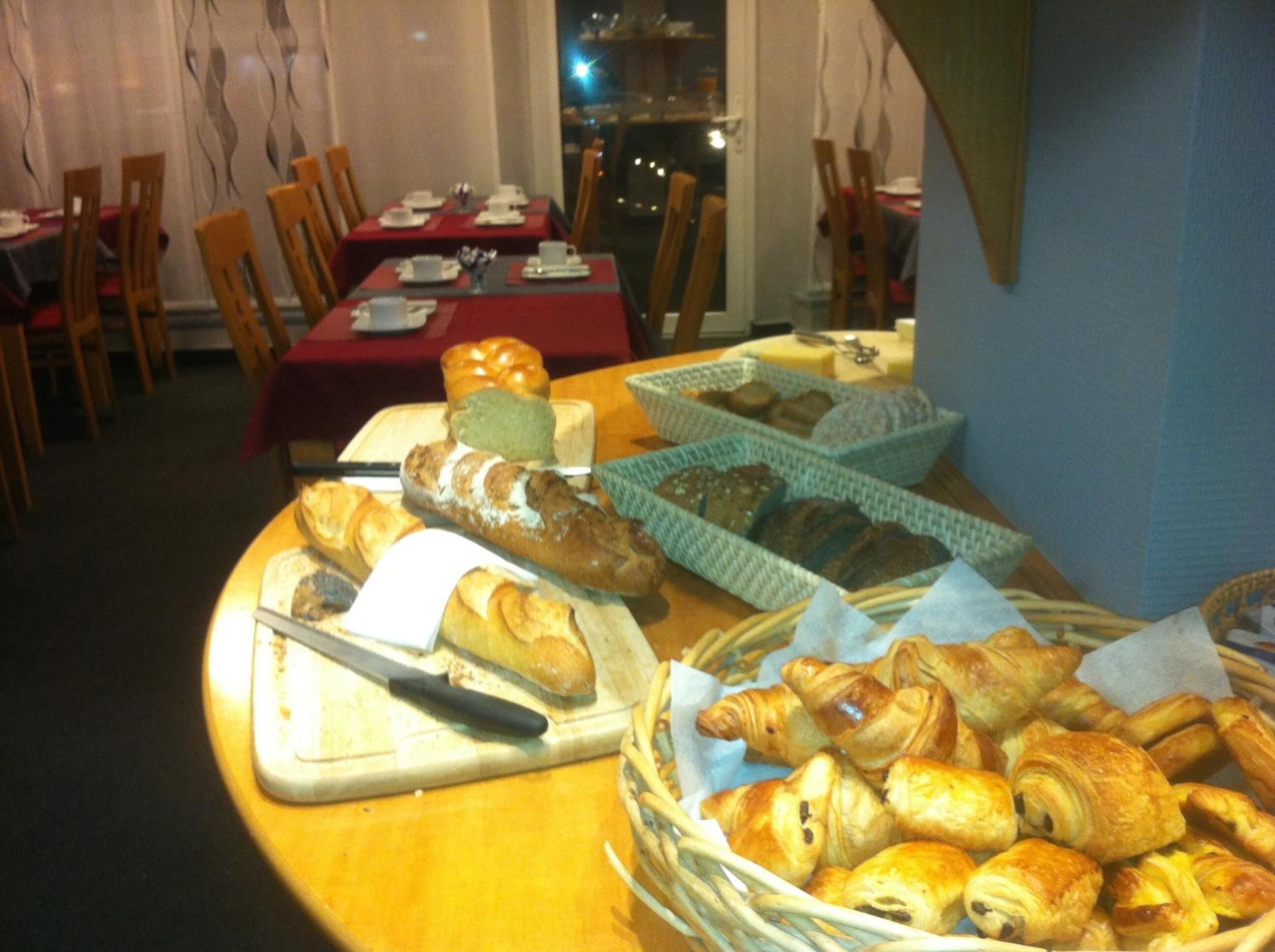 Un buffet de petit-déjeuner proposant diverses pâtisseries et pains, des tables recouvertes de nappes rouges et des chaises disposées autour de ces tables.