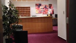 A reception area with a wooden desk, a plant, and artwork on the wall.
