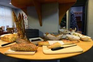 A table with various breads and pastries, a cutting board, and a knife. - Amadeus Hôtel (Sarreguemines)
