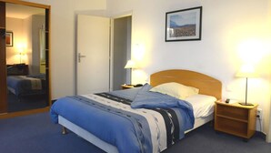 A hotel room with a bed, two bedside lamps, a framed picture on the wall, and a mirror on the door.