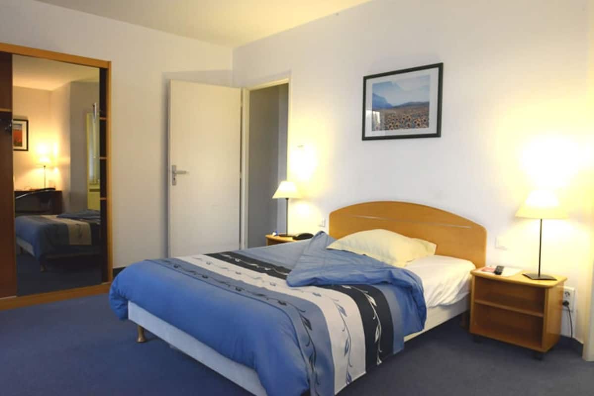 Une chambre d’hôtel avec un lit, deux lampes de chevet, un tableau encadré au mur et un miroir sur la porte.