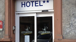A hotel entrance with a double door, a sign above reading "HOTEL", and the name "amadeus" on the glass doors.