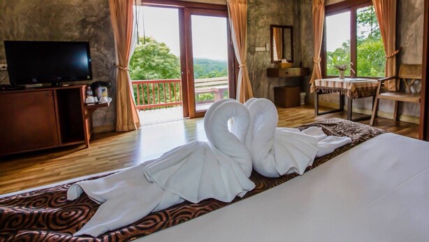 Habitación de hotel con cama, televisión, escritorio y balcón con cortinas.