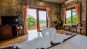 Habitación de hotel con cama, televisión, escritorio y balcón con cortinas.