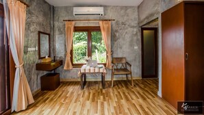 Una habitación con suelo de madera, una silla de madera, una mesita con un ordenador portátil, un lavabo y una ventana con cortinas.