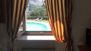 A window with striped curtains, a pool, and a view of a bridge and hills. - Colle Sul Lago (Cingoli)