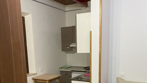 A compact kitchen with a built-in oven, a small table, and a sofa. - Colle Sul Lago (Cingoli)