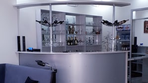 A modern bar area with a curved counter, shelves with glassware, and a seating area with a sofa and armchair. - Hotel Rio (Tbilisi)