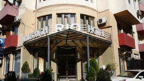 A hotel entrance with a covered entrance, potted plants, and a white car parked outside. - Hotel Rio (Tbilisi)