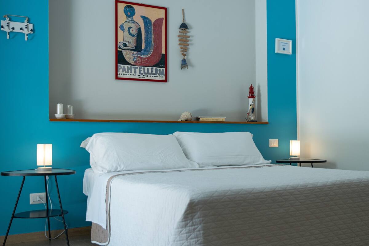 A bedroom with a bed, two bedside tables, a wall-mounted shelf, and a decorative item.
